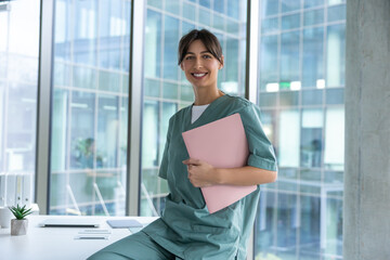 Smiling dark-haired female doctor in lab coat with a medical history in hands