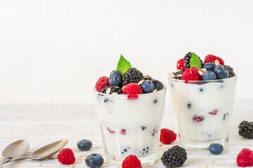 Greek yogurt with fresh berries, oats and mint in glasses with spoons on white background. Creamy...