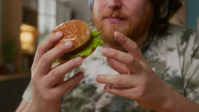 Close-up shot of man with beard and headphones holding small delicious burger and felling excited to try it