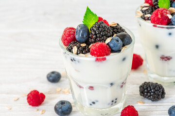 Creamy Greek yogurt with fresh berries, oats and mint in glasses on white background. Yoghurt topped with blueberry, raspberry, blackberry and granola. Healthy breakfast. Close up. Summer diet food
