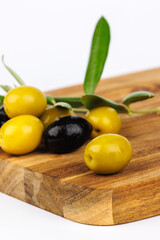 Assorted green and black olives and olive twigs on rustic wood board over white base