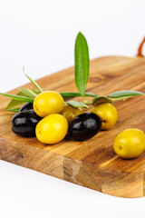 Green and black olives with olive twigs on wooden cutting board on white surface
