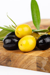 Green and black olives and olive twigs on cutting board with white background