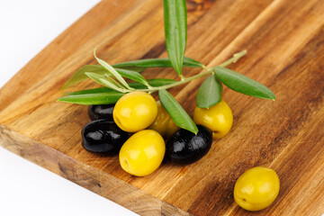 Mediterranean olives and olive branches arranged on wooden board on white backdrop