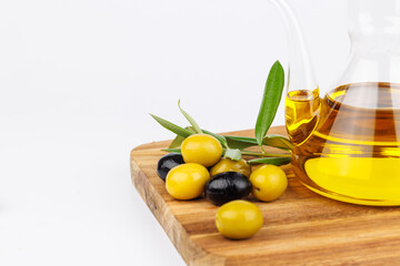 Rustic scene with olive oil cruet, fresh green olives and olive twigs on a dark chopping board,...