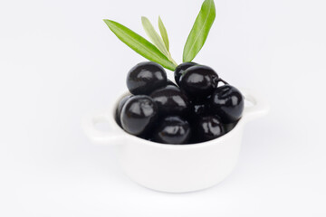White bowl with black olives and olive branch on white background, Mediterranean food still life, top view minimal composition