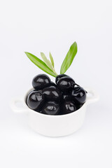 Black olives in ceramic bowl with olive twig on clean white backdrop, Mediterranean diet ingredient concept, top view