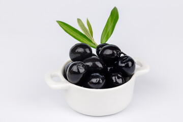Minimalist top view of black olives in white bowl with olive branch on plain white background, healthy Mediterranean snack
