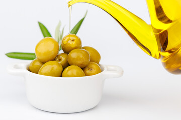 Fresh green olives in white bowl with olive oil dispenser pouring oil and olive branch on clean...