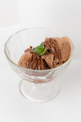 Two scoops of chocolate ice cream in a clear dish, drizzled with fudge and mint