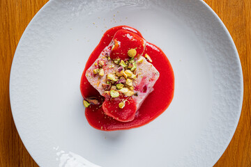 A stunning dessert on a white plate, topped with nuts and berry sauce for extra appeal