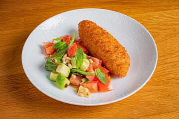 Golden croquette rests beside a vibrant salad with tomatoes and herbs, showcasing culinary art