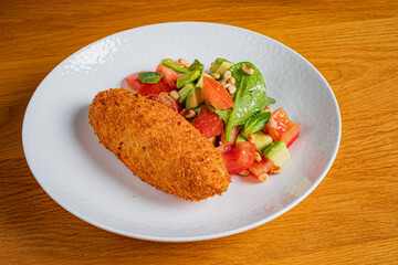 A golden-brown croquette rests next to a vibrant salad of tomatoes, spinach, and avocado