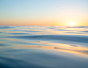 Obraz premium Gentle ripples of water reflecting soft orange sunlight under a pale blue sky.
