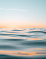Fototapeta premium Gentle ripples of water reflecting soft orange sunlight under a pale blue sky.