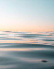 Fototapeta premium Gentle ripples of water reflecting soft orange sunlight under a pale blue sky.