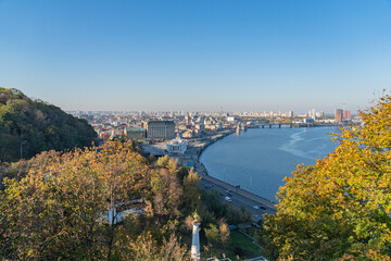 A panoramic cityscape view from an elevated vantage point, showcasing a mix of architectural styles, parks along a tranquil river cutting through the city The image suggests fall season with autumna