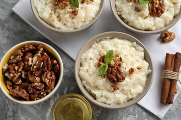 Delicious rice pudding with walnuts, cinnamon, mint and honey on grey table, flat lay