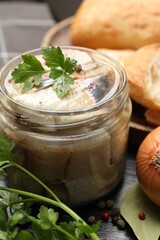 Pieces of delicious herring with spices and parsley in jar on black table, closeup