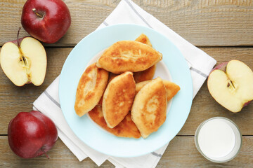 Delicious fried pyrizhky (stuffed pies) with apples and milk on wooden table, flat lay
