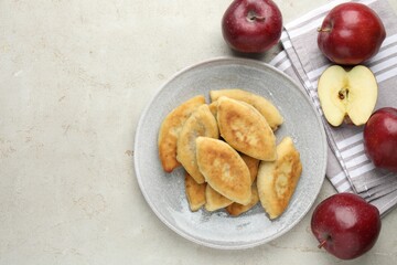 Delicious fried pyrizhky (stuffed pies) and apples on light grey table, flat lay. Space for text