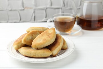 Delicious fried pyrizhky (stuffed pies) and tea on white wooden table, closeup