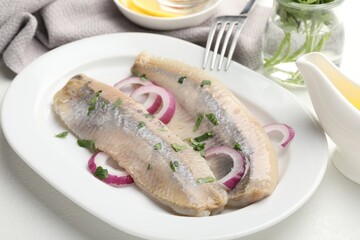 Tasty herring fillets with onions and parsley served on white table, closeup