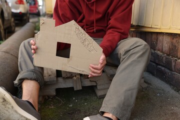Homeless man with carton house figure outdoors, closeup