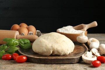 Making pizza. Different ingredients on wooden table against black background, closeup