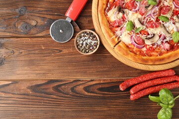 Tasty pizza with smoked sausages, ingredients and cutter on wooden table, flat lay. Space for text