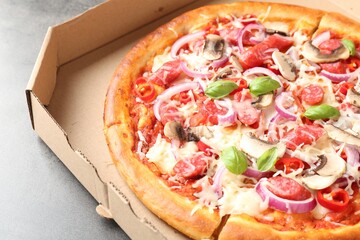Tasty pizza with smoked sausages and mushrooms in cardboard box on gray table, closeup
