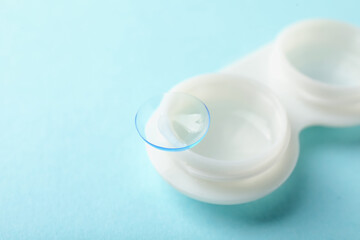 Contact lenses and case on light turquoise background, closeup. Space for text