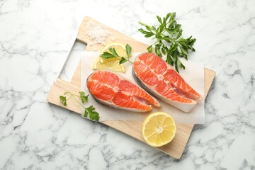 Seafood. Fresh raw salmon steaks, parsley, pieces of lemon and salt on white marble table, top view