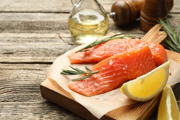 Seafood. Pieces of salmon fillet, spices, oil and lemon wedges on wooden table, closeup