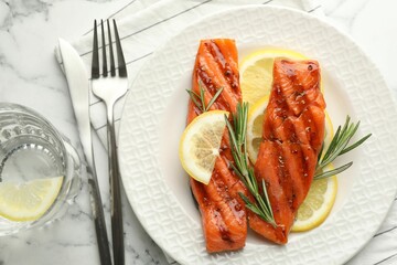 Seafood. Tasty grilled salmon served with water, cutlery, rosemary and lemon on white marble table, flat lay