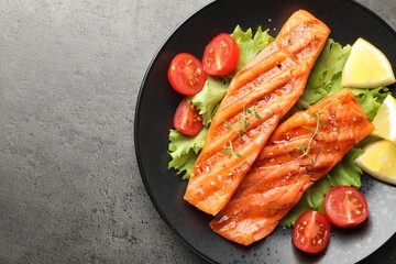 Tasty grilled salmon served with lettuce, tomatoes and lemon on grey table, top view. Space for text