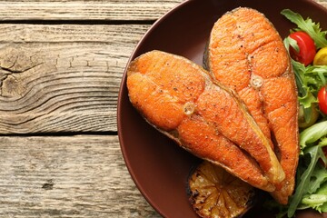 Seafood. Tasty salmon steaks served with salad and lemon on wooden table, top view. Space for text