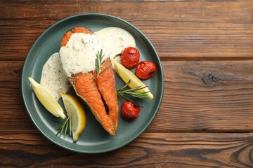 Seafood. Tasty salmon steak served with sauce, tomatoes, rosemary and lemon on wooden table, top...