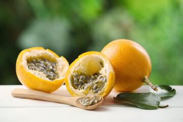 Ripe passion fruits, green leaves and seeds on white wooden table outdoors, closeup