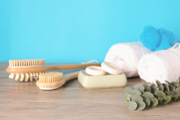 Different bath accessories and eucalyptus branch on wooden table against light blue background, closeup
