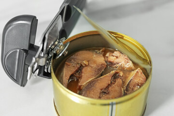 Can opener and tin with fish on white table, closeup