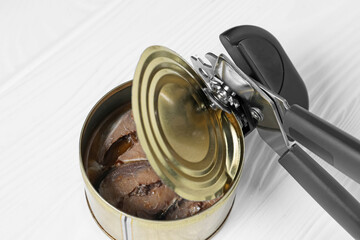 Can opener and tin with fish on white wooden table, above view