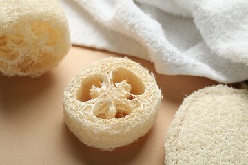 Natural loofah sponges and towel on beige background, closeup