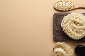 Natural loofah sponges, cosmetic product, towel and brush on beige background, flat lay. Space for text
