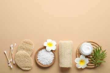 Natural loofah sponges, cosmetic product, sea salt, swabs, plumeria flowers and green twig on beige background, flat lay. Space for text