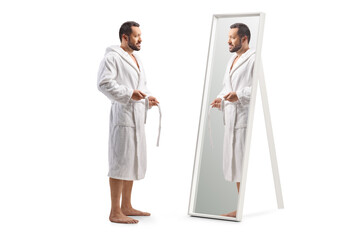 Full length profile shot of a man putting on a bathrobe in front of a mirror