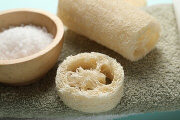 Natural loofah sponges, sea salt and towel on table, closeup