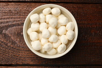 Tasty mozzarella cheese balls in bowl on wooden table, top view