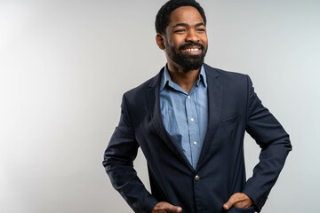 Smiling handsome black man in suit posing confidently in studio, standing with hands in jacket pockets, friendly and professional expression on neutral background.