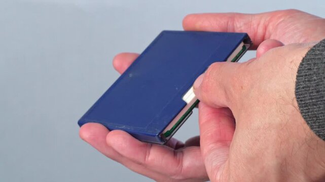 A close-up shot of two hands inserting a white MiniDisc into its blue protective case. The fingers carefully guide the disc into the sleeve. This footage evokes a sense of nostalgia
